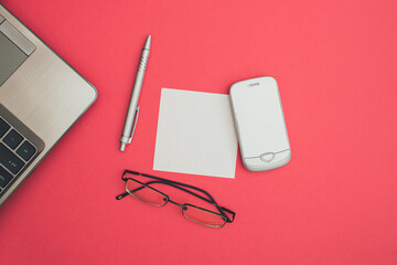 Business Square leaflet mock up blank template design idea. Gray laptop, mobile phone, glasses and ballpoint pen mockup against pastel pink background. Copy space templates designs for message layout.