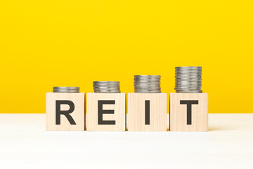 reit text written on wooden block with stacked coins on yellow background