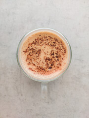 A glass cup with double wall of coffee. The hot drinkin a transparent mug, on a gray background, isolated. Hot chocolate with light foam and cocoa powder, top view.