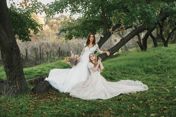 lesbian couple of beautiful young women in love in white wedding dresses posing on a meadow in the forest.