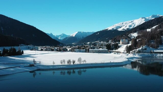 2022 - Excellent aerial view approaching snowy Davos, Switzerland over a lake.
