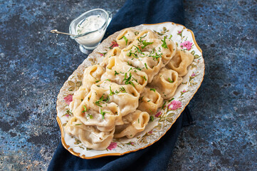 Oriental traditional food - Manty with minced beef or lamb meat in a plate with sauce on a blue background.