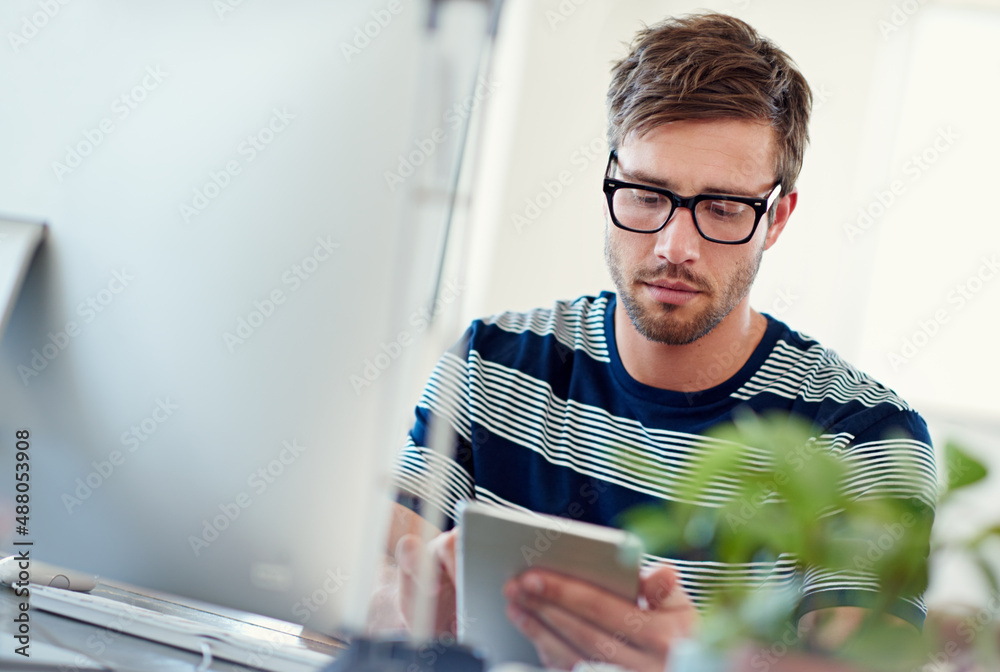 Poster this site needs some work. shot of a casually-dressed young man using a digital tablet at his desk.