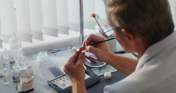 Close-up of painting a ceramic dental crown with a thin brush by hand