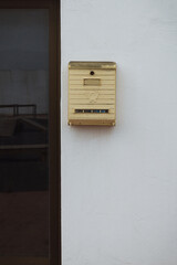 Old rusted yellow mailbox on an aged white background wall with cracks and concrete texture. Post box.