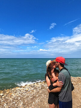 Couple in love kissing in the sea, young woman with a hat and young man with a cap in the sea.