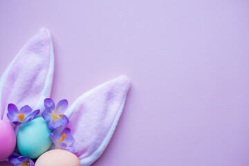 bunny ears, easter eggs and spring flowers on a lilac background. simple minimalism flat lay top view copy space
