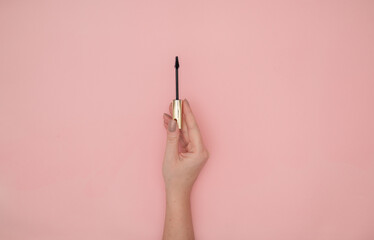 Woman hand holding an eyelash mascara on a pink background with copy space