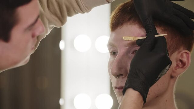 A man eyebrow master waxing the hairs on eyebrow of