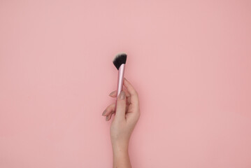 Woman hand holding a make up brush on a pink background with copy space, top view