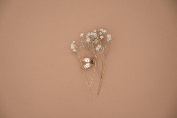 Wedding ring and dried baby’s breath flowers on beige background.