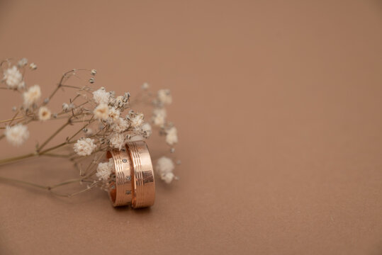 Wedding ring and dried baby&rsquo;s breath flowers on beige background.