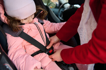 Cropped image of a caring mom fastening her adorable little daughter's seat belt. Safe movement of children in the car, auto security and safety travel by car concept.