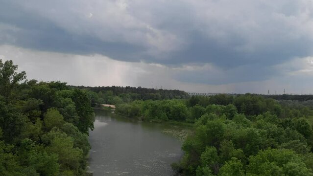 An aerial view of the lake from a bird's eye view before a thunderstorm begins. Aerial view from a drone flying over a field along a lake before a summer thunderstorm. Natural background in 4K resolut