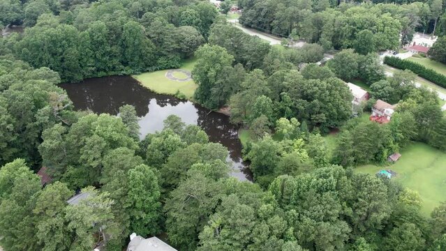 Aerial drone pull away from brown lake summer time with green trees neighborhood