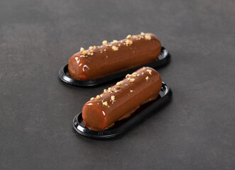 Energy Chocolate walnut cake in the form of a cylindrical bar, with mirror glaze on a serving plate on a dark background
