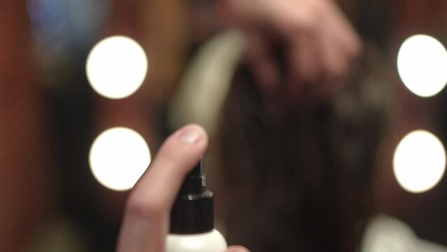 Close-up spraying hair fixation spray in slow motion indoors. Unrecognizable Caucasian man doing hairstyling for female client in beauty salon. Hairdo and service concept