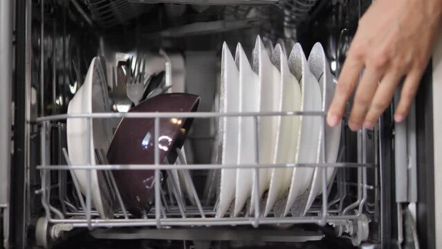 Adding dishes into the dishwasher machine. Arranged dishes into the dish washer.