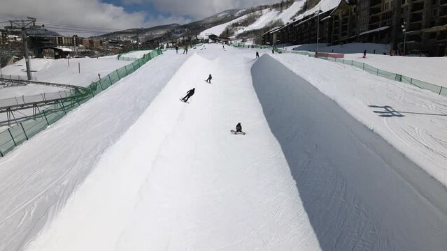 2022 - Excellent aerial view of people skiing and snowboarding on a half-pipe at Steamboat Springs, Colorado. One snowboarder falls.