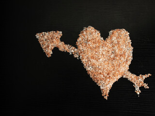 Himalayan pink salt, in the shape of a heart with an arrow and a black background