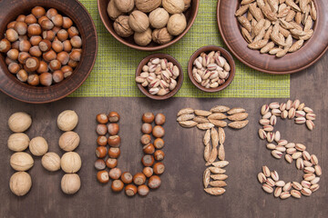 Word nuts from different type of nut. Walnut, hazelnut, almond, pistachio on brown and green background, top view, flatlay