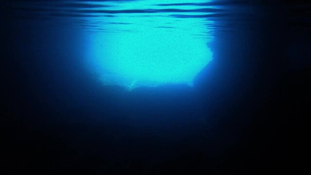 Underwater view of the entrance of a sea cave withe the flashy blue light reflecting under the waving surface, Vis island, Adriatic Sea, Croatia