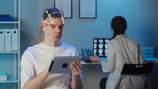 EEG topographer for examining brain, doctor making electrogram of scalp activity. Researching of brain work, man using gadget wearing electroencephalography headset.