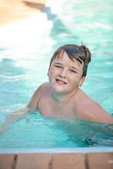 Fototapeta na wymiar Happy pre-teen boy swimming in backyard pool