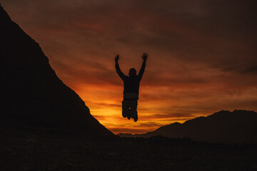 silhouette of a person jumping on the top of mountain