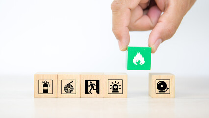Hand choose cube wooden block stack with fire icon and door exit sing or fire escape with prevent icon and fire extinguisher and emergency protection symbol for safety and rescue.