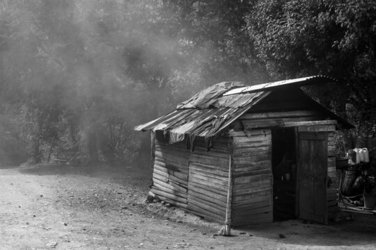 Dramatic black and white image of a old wooden weathered cooking shack high in the Caribbean mountains with clothes drying on the hot metal roof.