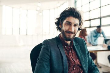 One of the best companys to work forOne of the best companys to work for. Portrait of a young businessman sitting in a modern office with his colleagues working in the background.