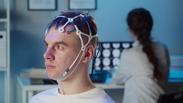 Man wearing EEG topographer for examining brain, doctor making electrogram of scalp activity. Researching of brain work using electroencephalography headset.