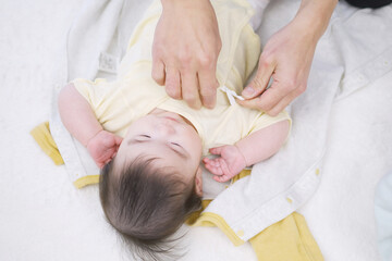 Obraz na płótnie Canvas 赤ちゃんのお着替えをするアジア人のお父さん 