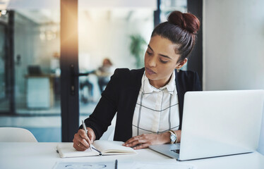 Success is a consistent, daily effort. Shot of a young businesswoman making notes at her desk in a modern office.