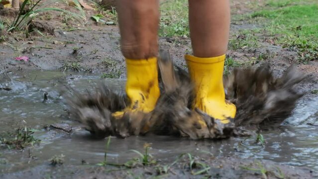 Close-up of the feet of a happy little girl in rubber boots jumping in a puddle. Child's feet in the muddy