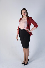 A cute plus-size model stands on a pink background in a red unbuttoned jacket, a pink blouse with lace, a black office skirt and high-heeled shoes. A modest business portrait