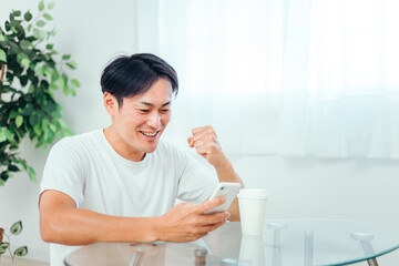 部屋でスマホを見る男性（ガッツポーズ）
