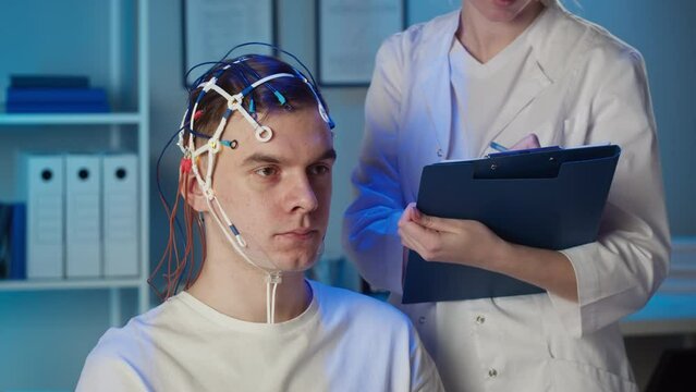 EEG topographer for examining brain, doctor making electrogram of scalp activity. Researching of brain work man wearing electroencephalography headset and holding cube.