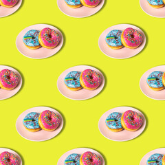 A repeating pattern of pink and blue donuts with a rainbow on a plate on a yellow background. Flat lay