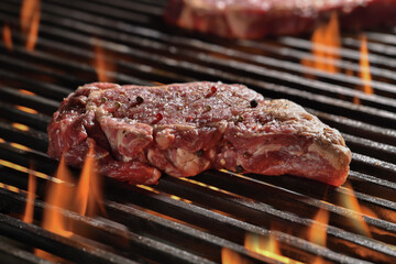 Raw seansoned rib-eye steaks meat beef cooking on flaming grill.