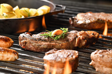 Cooked juicy steak meat beef with garlic and seasoning on top on a flaming grill surrounded by other meat and sausages.