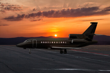 Black executive corporate business jet at the airport apron on the background of a picturesque sunset