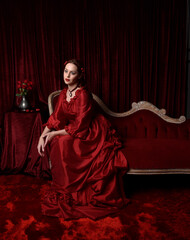   portrait of pretty female model with red hair wearing glamorous historical victorian red ballgown.  Posing with a moody dark background.