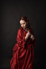  portrait of pretty female model with red hair wearing glamorous historical victorian red ballgown.  Posing with a moody dark background.