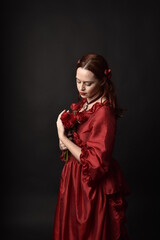   portrait of pretty female model with red hair wearing glamorous historical victorian red ballgown.  Posing with a moody dark background.