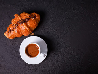 Fresh baked croissant, white mug of expresso on black concrete table. Cup of hot coffee, buns, rolls close up. Food, French breakfast, morning menu, cafe concept. Top view, copy space