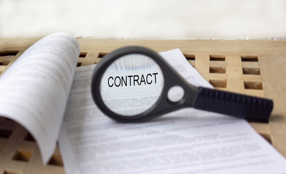 Close-up through a magnifying glass of a verbal contract on a wooden background. Selective focus.