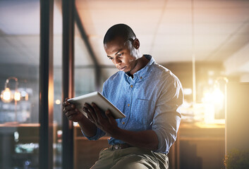 In make things happen mode. Shot of a young businessman using a digital tablet during a late night in a modern office.