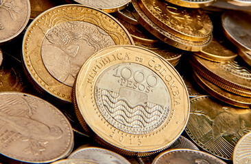 monedas de mil pesos colombianos sobre un montón de otras monedas de mas bajo valor comercial  - obrazy, fototapety, plakaty